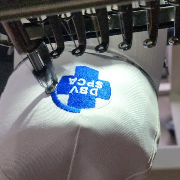 A white cap being embroidered by Cotton Polly